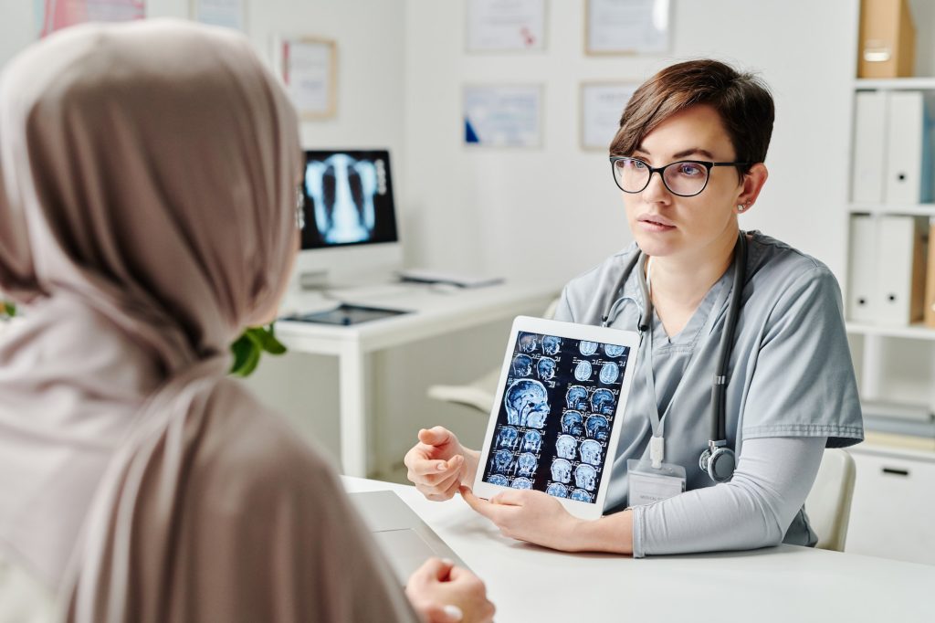 Young confident radiologist in uniform commenting brain scan to patient